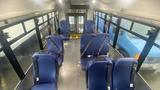 Interior view of a 2021 Ford Transit with several blue seats and safety belts arranged in rows facing the aisle