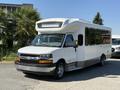 A 2017 Chevrolet Express shuttle bus with a white exterior and a raised front roof is parked with large windows on the side and chrome accents on the front grille