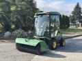 A 2021 John Deere 1575 lawn tractor with a clear cab and a large front brush attachment is parked on a driveway