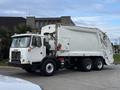 A 2010 Autocar Xpeditor garbage truck with a white body and large rear loading mechanism parked on the street