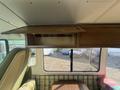 A 1976 GMC Motorhome interior featuring green upholstered seating a wooden overhead storage compartment and a plaid patterned bench seat with a table in the center