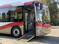 A 2016 Grande West Vicinity bus with a red and white exterior features an open entrance and a wheelchair ramp deployed on the side