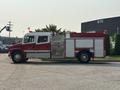 A red 1999 Freightliner FL80 fire truck with emergency lights and markings is parked on a street with a long chassis and various compartments for equipment