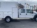 A 2015 Ford F-550 with a large service body and multiple compartments on the side, featuring a white exterior and a crew cab design