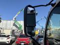 A side mirror of a 2018 Hino 195 truck showing a reflection of surrounding vehicles and machinery