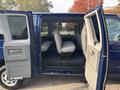 A blue 2013 Ford E-350 Super Duty van with wide-open passenger doors revealing grey seats and a spacious interior