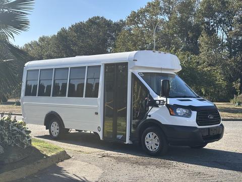 A white 2017 Ford Transit-350 bus with large windows and a side entry door is parked on the street