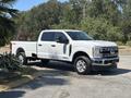 A 2023 Ford F-350 Super Duty pickup truck in white with a crew cab and chrome wheels parked to the side