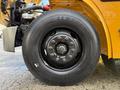 Close-up of a black tire mounted on a yellow school bus featuring visible wheel studs and a prominent brand name on the sidewall