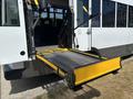 A 2020 Chevrolet Express bus with a fold-out wheelchair lift extended from the rear door featuring a textured surface and safety bars attached at both sides