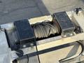 A winch with a spool of thick steel cable mounted on a platform with two black housing units and a hook attachment