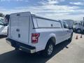 A white 2019 Ford F-150 pickup truck with a covered bed and a toolbox mounted on the rear is parked in a lot
