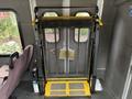 A 2014 Ford E-350 with a wheelchair lift in the open position featuring a yellow and black design and a mesh safety barrier