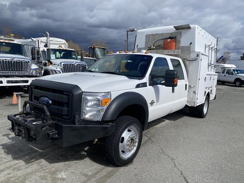 A white 2015 Ford F-550 truck with a flatbed and utility box on the back, featuring an armored grille and orange lights on top
