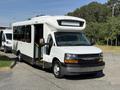 A 2017 Chevrolet Express bus with a white exterior and a large front windshield is parked with its front door open