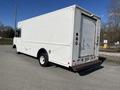 A white 2012 Ford Econoline delivery van with a rear roll-up door and round tail lights parked on a gravel surface