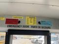Interior view of a bus showing signs for emergency procedures responsibilities and service instructions with a focus on the emergency door