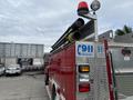 A red 2002 GMC C7500 fire truck with metal storage compartments and a light bar on top equipped with black hoses
