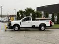 A 2023 Ford F-250 pickup truck with a plow attached in white parked on a concrete surface