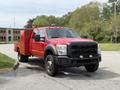 A red 2013 Ford F-550 truck with a utility body and black front grille is parked on a paved surface showcasing its large tires and headlights