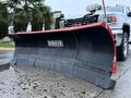 A red and black snow plow with a curved blade mounted on a white 2017 GMC Sierra 3500HD pickup truck
