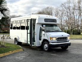 A 2002 Ford Econoline bus parked with its door open showcasing a white exterior and large windows