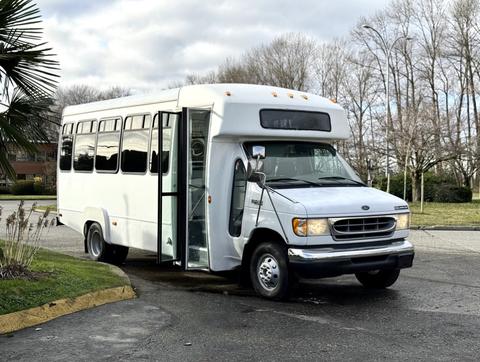 A 2002 Ford Econoline bus parked with its door open showcasing a white exterior and large windows