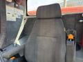 A gray fabric operator's chair with armrest controls and a safety harness in a vehicle's cabin designed for drilling operations