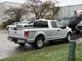 A silver 2015 Ford F-150 pickup truck parked on a wet surface with a visible 4x4 badge on the tailgate and chrome accents on the rear wheels