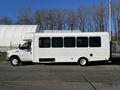 A white 2014 Ford Econoline shuttle bus with large windows on the side and single rear wheels