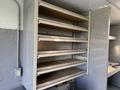 A shelving unit with multiple horizontal shelves in a vehicle interior designed for storage and organization. The unit is mounted against a wall and has a simple, functional design