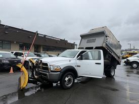 A 2011 Dodge Ram 5500 dump truck with a plow attached in the front and the dump bed raised