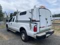 A white 2014 Ford F-350 Super Duty pickup truck with a utility service body and ladder racks on the bed the rear has reflective tape and an orange light bar
