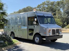 A 2009 Morgan Olson Workhorse W62 delivery truck with a silver exterior featuring multiple side compartments and a large front windshield