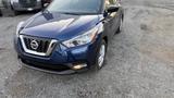 A blue 2019 Nissan Kicks parked on gravel featuring a distinctive front grille and sleek design with halogen headlights and stylish curves