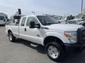 A white 2014 Ford F-250 Super Duty truck with a crew cab and chrome wheels is parked at an angle showing its front and side profile