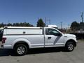 A white 2019 Ford F-150 truck with a camper shell on the bed is parked with no visible cargo attached
