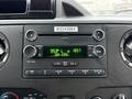 A close-up view of the dashboard of a 2013 Ford E-350 featuring a radio display with frequency and time indicators along with various control knobs and buttons