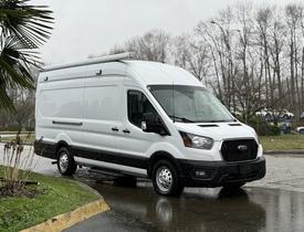 A white 2023 Ford Transit van with a black front grille and a plain side design parked on a wet surface