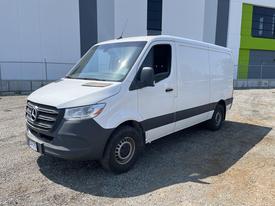 A 2022 Mercedes-Benz Sprinter van with a white exterior and black accents parked at a location with gravel ground