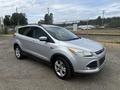 A silver 2014 Ford Escape parked on gravel with a shiny exterior and alloy wheels