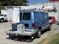 A blue 2006 Ford Econoline van equipped with a utility ladder and a white storage box mounted on the rear with reflective markings