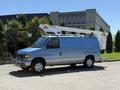 A blue 2006 Ford Econoline van with a bucket truck attachment on the roof parked on the street