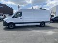 A 2025 Mercedes-Benz Sprinter van in white with a black stripe along the bottom parked on a lot featuring large wheels and a sleek design