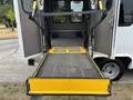 A 2014 Ford E-350 with a folded wheelchair ramp extending from the rear doors with a textured metal surface and yellow safety edges