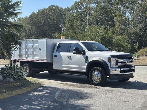 A 2019 Ford F-550 truck with a flatbed and side rails is parked with an orange light on the roof