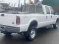 A white 2005 Ford F-350 SD pickup truck with a flatbed and silver metal rack on the back with four wheels and a prominent display of the Ford emblem