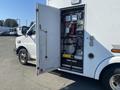 A 2011 Chevrolet Express with its side door open, revealing internal equipment and wiring mounted on the interior wall