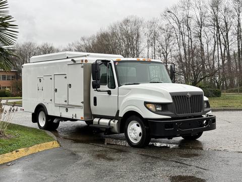 A 2014 International TerraStar is parked with a white exterior and a metallic service body featuring multiple compartments and a flatbed in front