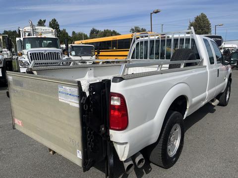 A white 2014 Ford F-250 SD pickup truck with a metal rack in the bed and a spare tire mounted against the side